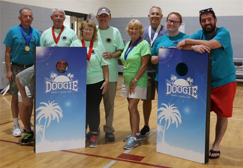 Group of cornhole players posing with boards and one man putting face through the hole smiling